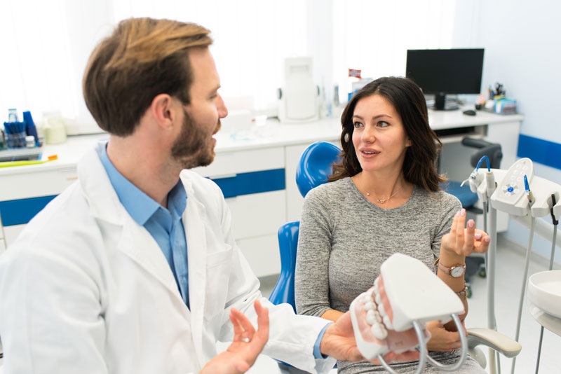 The image depicts a dental professional showing a dental model to a patient. The patient is attentively listening and engaged in the conversation.